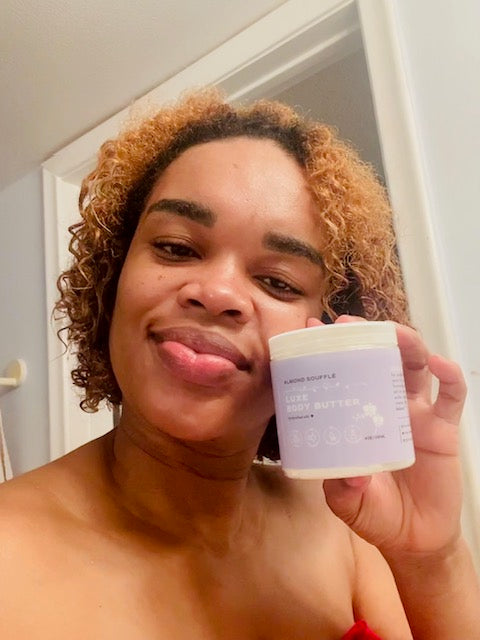 Black woman with curly gold hair holding a jar  of Zen & Bloom Almond Souffle  whipped body butter.